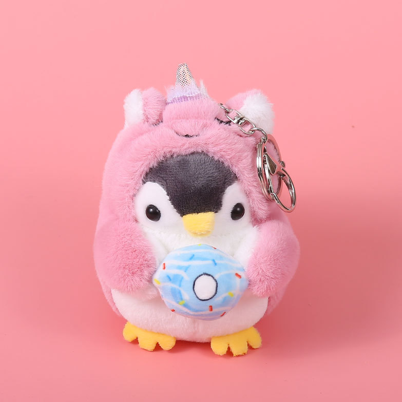 Kleiner Plüschpinguin, der ein rosafarbenes Einhornkostüm trägt und einen blauen Donut in den Händen hält.
