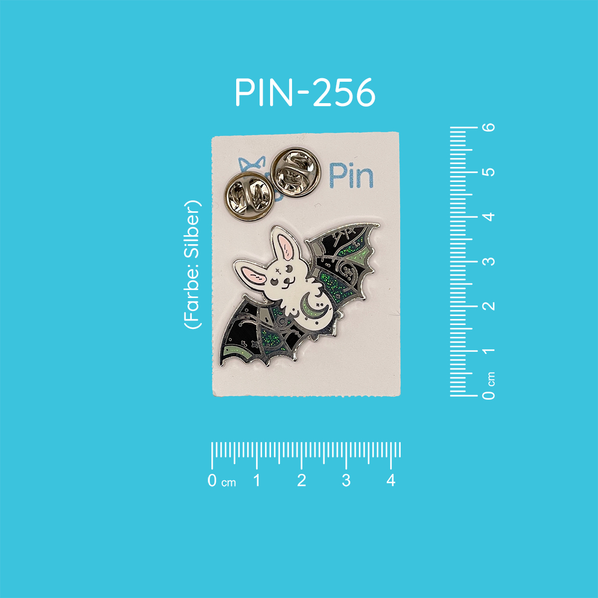 Pin mit dem Motiv einer weißen Fledermaus mit schwarz-grünen Flügeln mit Glitzer-Akzenten, auf deren Bauch ein grünlich-grauer glitzernder Mond abgebildet ist.