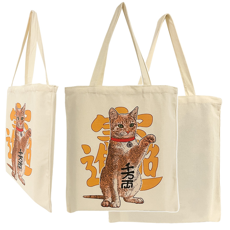 ES-22-001-1_0 Baumwolltasche mit dem Motiv einer sitzenden orange-weißen Katze, die eine Pfote anhebt. Hinter ihr und auf ihrem Bauch sind asiatische Schriftzeichen abgebildet.