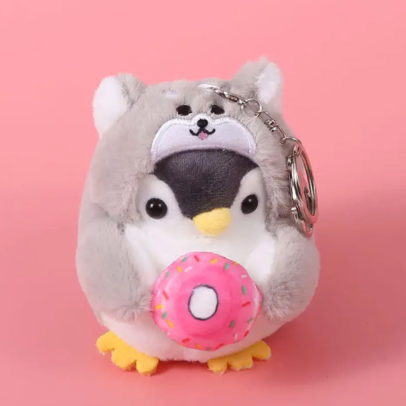 Kleiner Plüschpinguin, der ein graues Hundekostüm trägt und einen pinken Donut in den Händen hält.