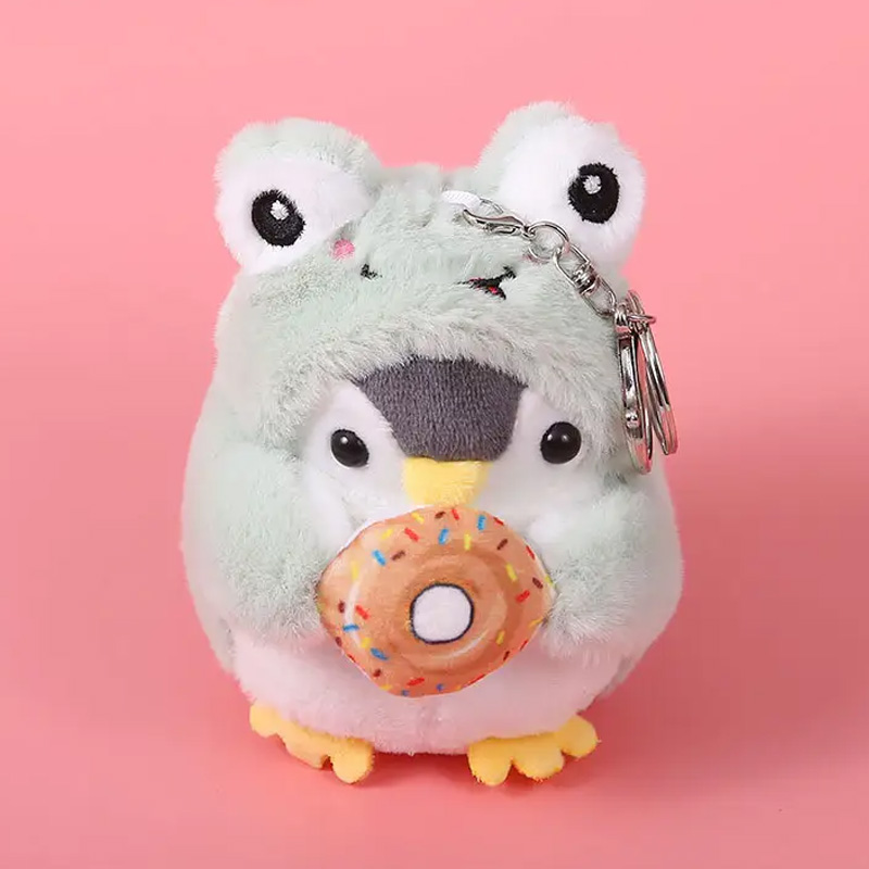 Kleiner Plüschpinguin, der ein grünes Froschkostüm trägt und einen braunen Donut in den Händen hält.