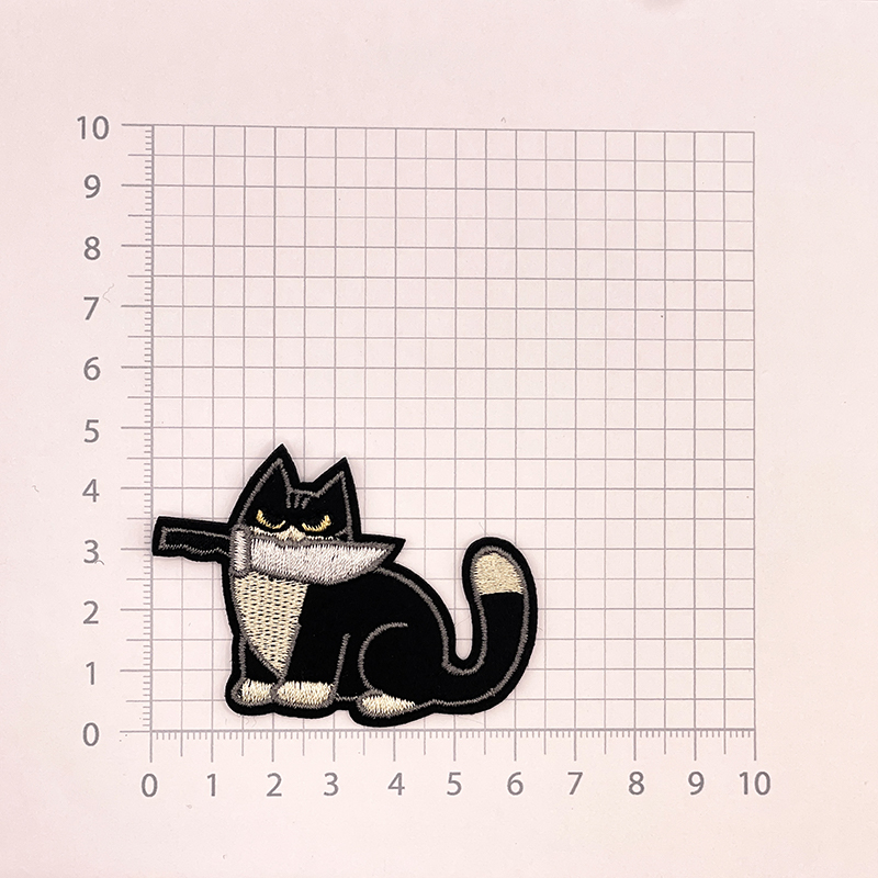 Aufnäher in Form einer Katze mit schwarzem Fell, die ein Messer im Mund hält.