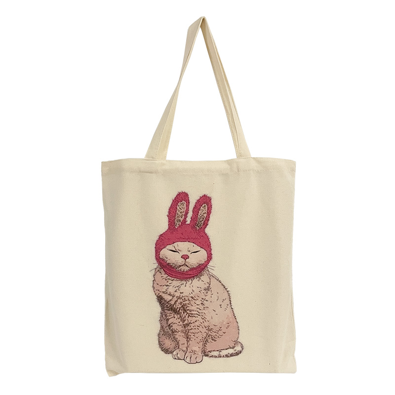 ES-22-001-6 Baumwolltasche mit dem Motiv einer beigefarbenen Katze mit einer roten Hasenohren-Mütze.